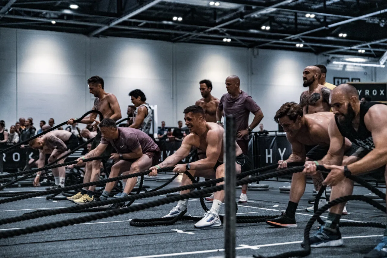 Hyrox competitors working a rope station side by side on the race floor