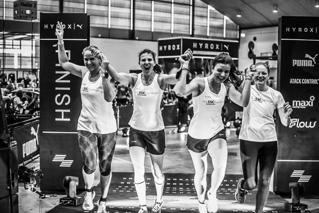 A Hyrox relay team crossing the finish line together with arms raised