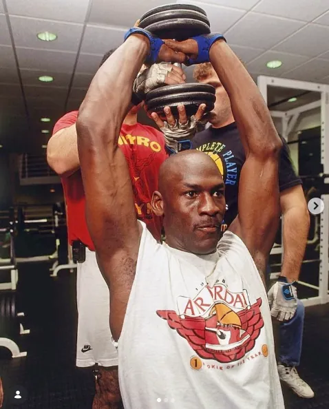 Tim Grover spotting Michael Jordan during an overhead dumbbell press